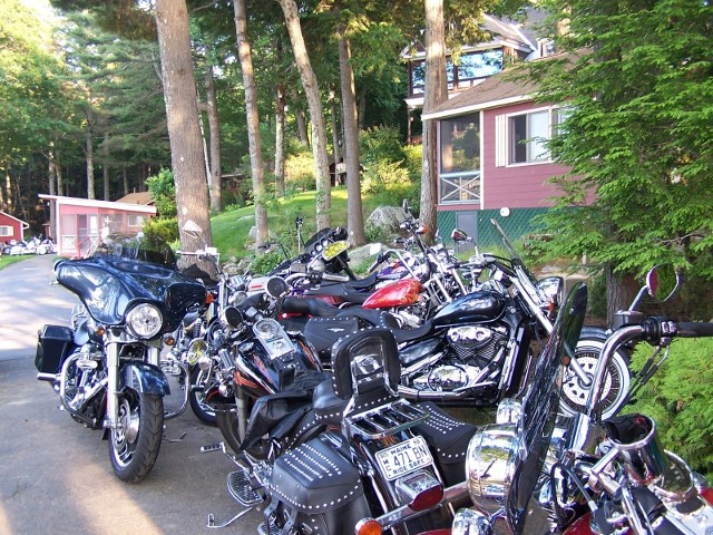 A group of motorcycles parked neatly in front of a residential house, showcasing various colors and styles.