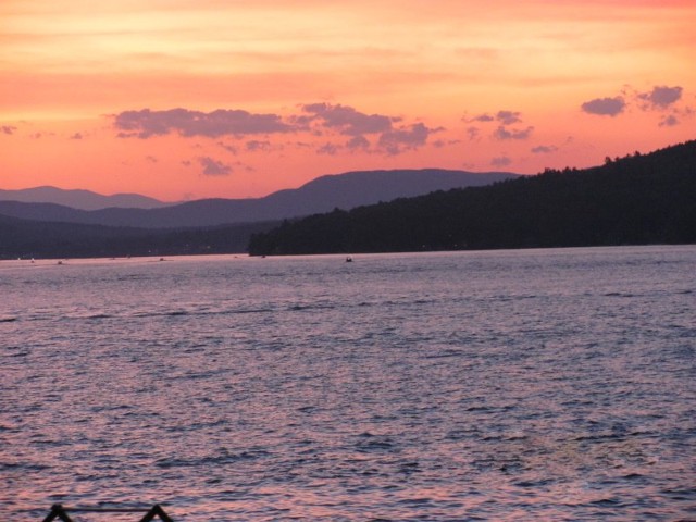 A vibrant sunset casts warm colors over water, with majestic mountains silhouetted in the background.