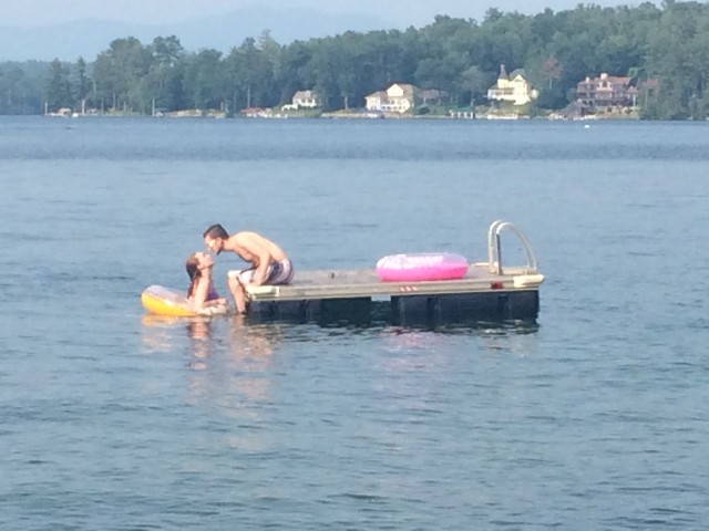 A couple stands on a wooden dock over calm water, enjoying a serene moment together.