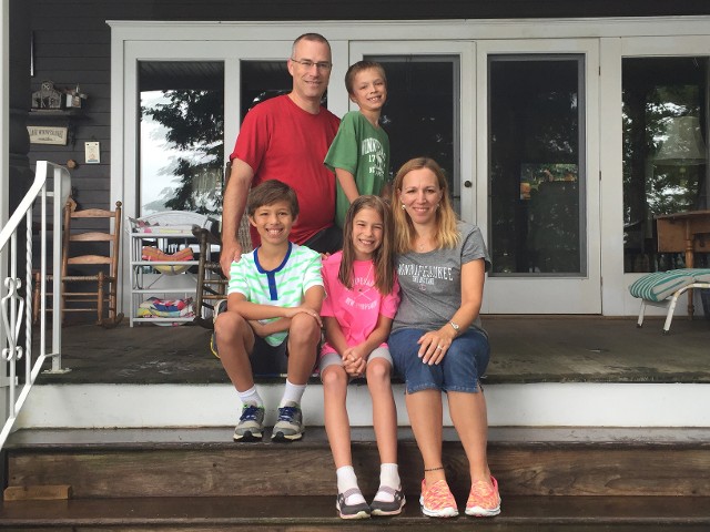 A family of four smiles together on the porch of their home, showcasing a warm and joyful moment.