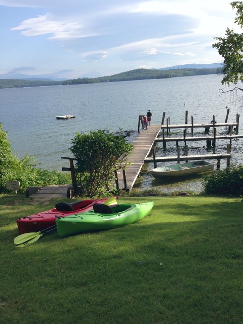 A green lawn featuring two kayaks beside a wooden dock, creating a serene outdoor setting by the water.