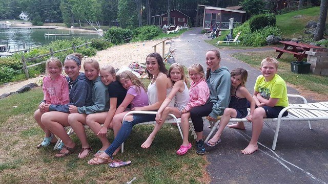 A group of girls sitting on a bench by the water, enjoying a sunny day and engaging in conversation.